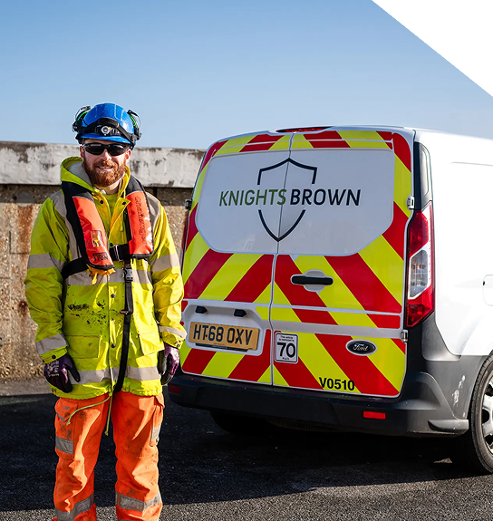 A highways technician standing infront of the back of his parked van, wearing a high vis jacket.